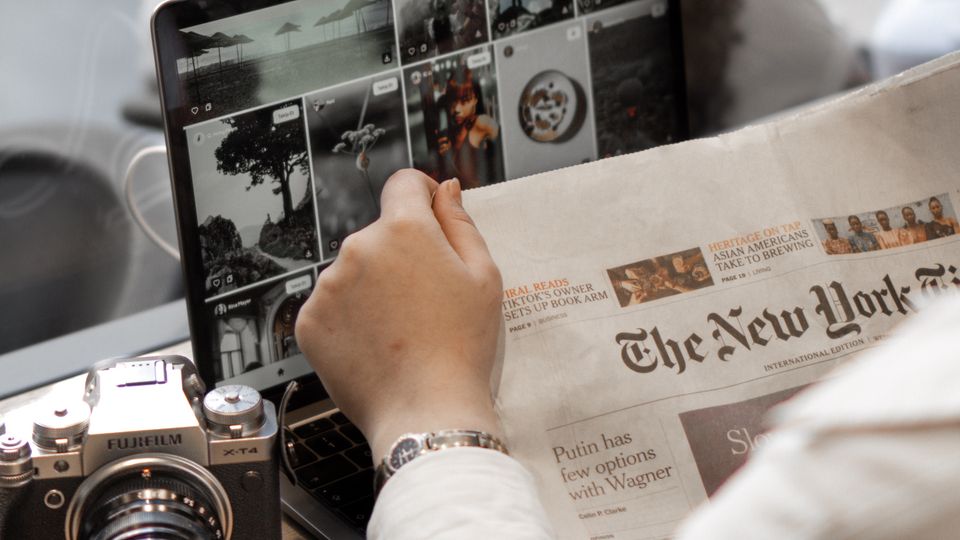Person reading a newspaper while working on a laptop